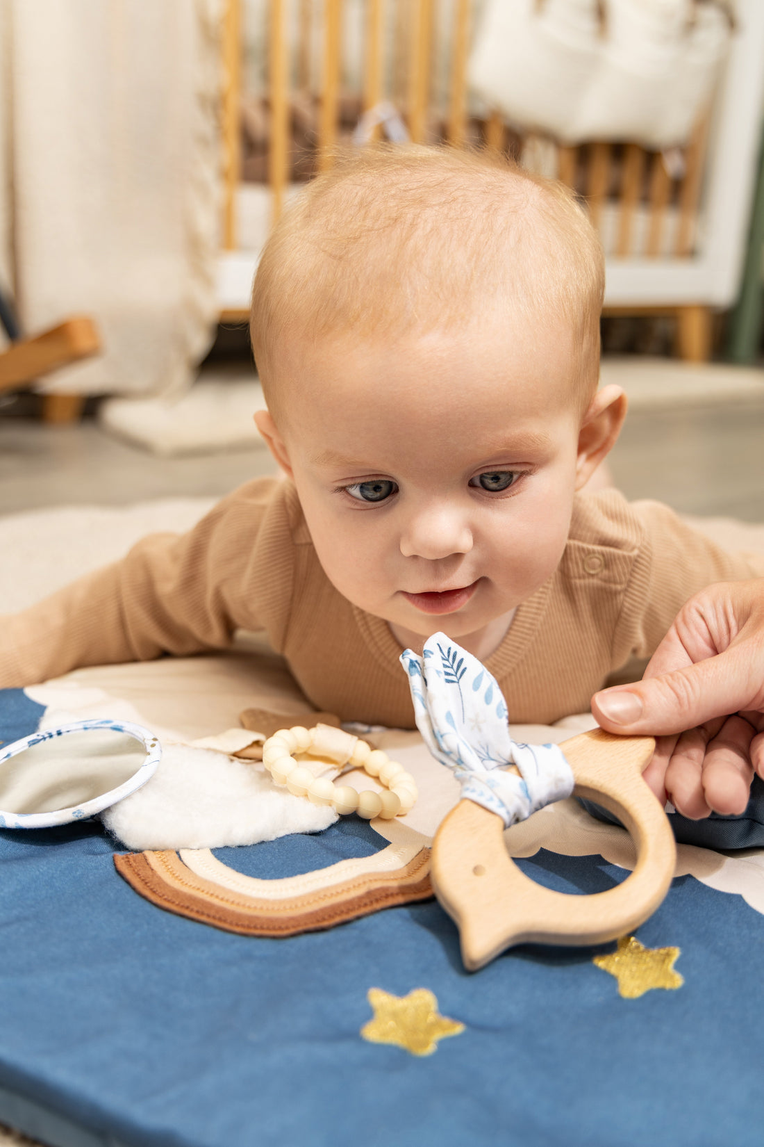 Bébé jouant sur le ventre dans une chambre avec un tapis d’éveil, un miroir et un anneau de dentition sensoriel.